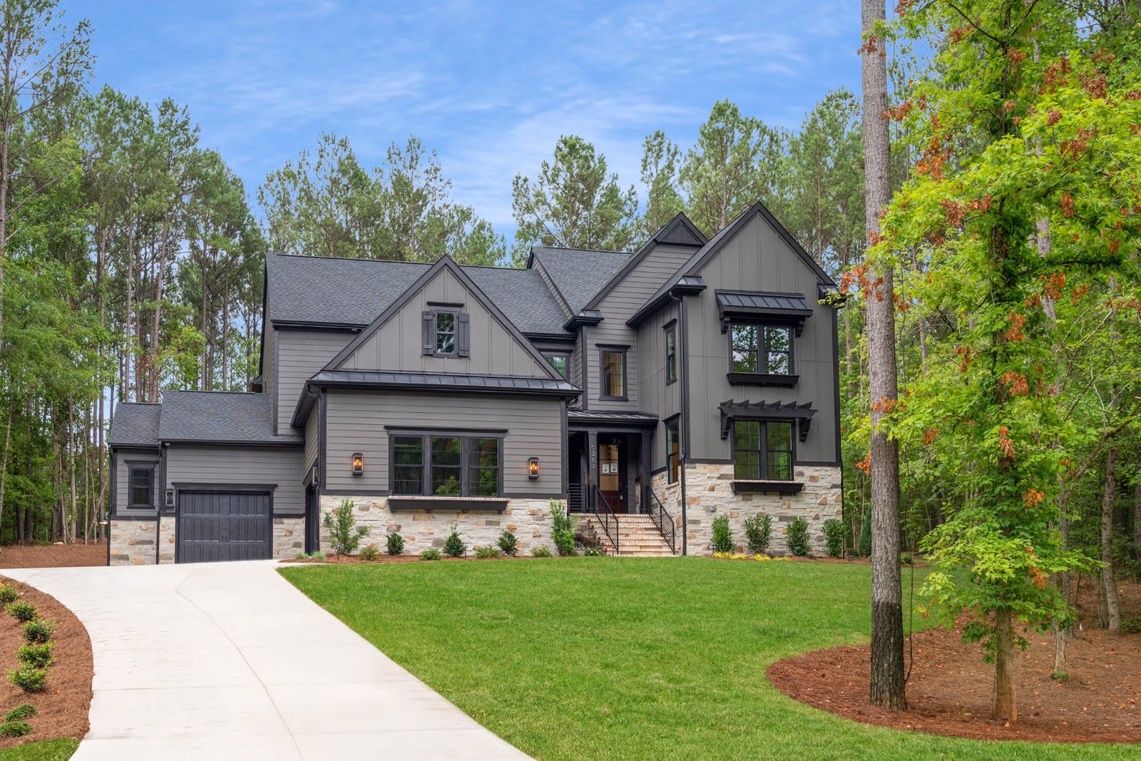 A charcoal-and-stone Carolina home at the end of a long white drive, tall pines behind