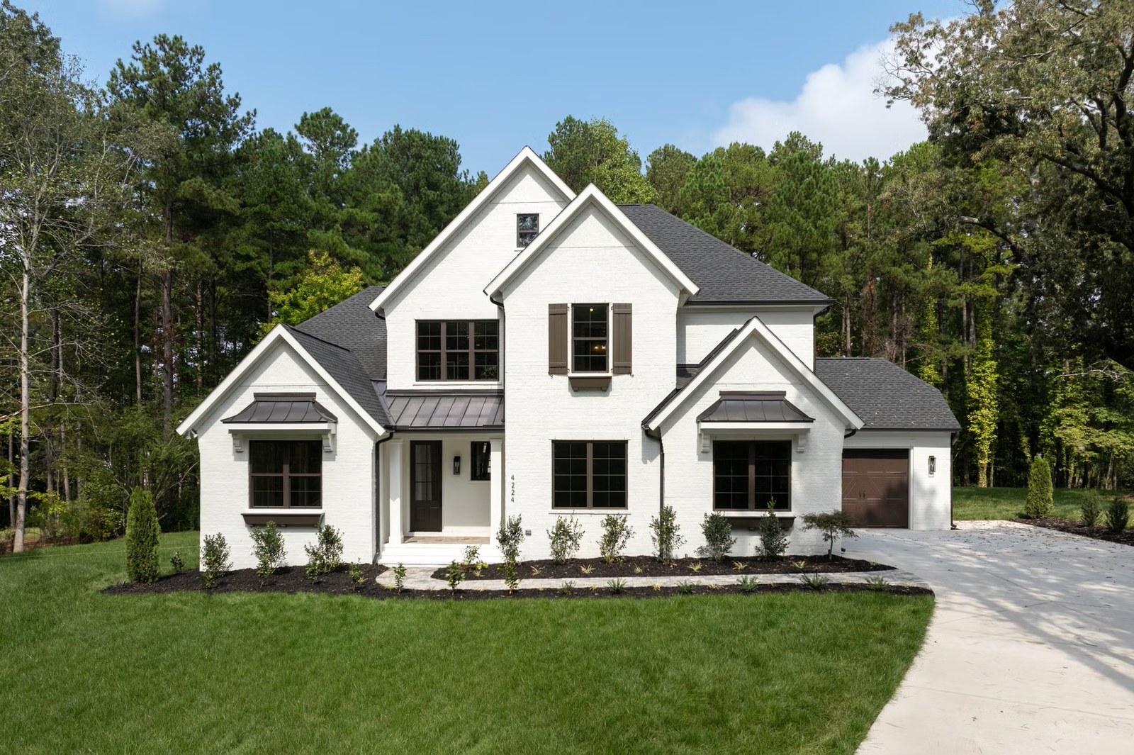 A crisp white farmhouse with a dark roof and pines behind