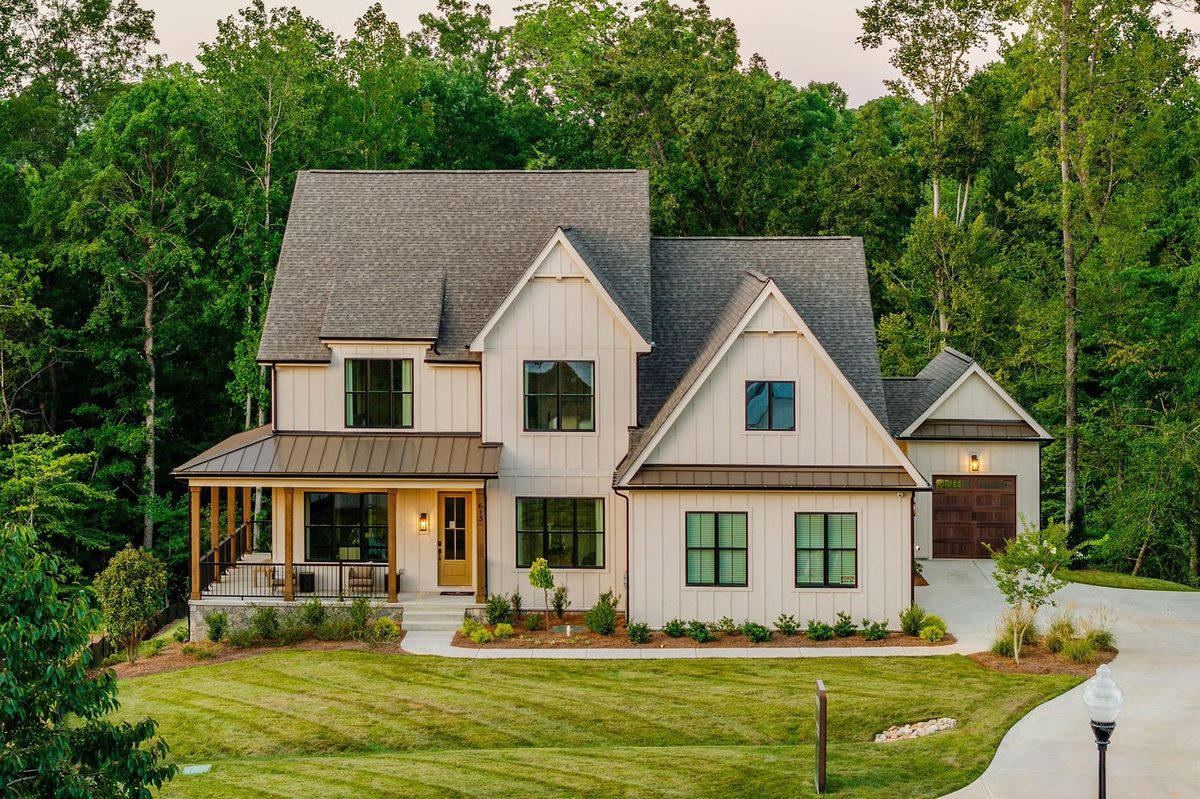 A cream farmhouse with a deep porch on a wooded lot