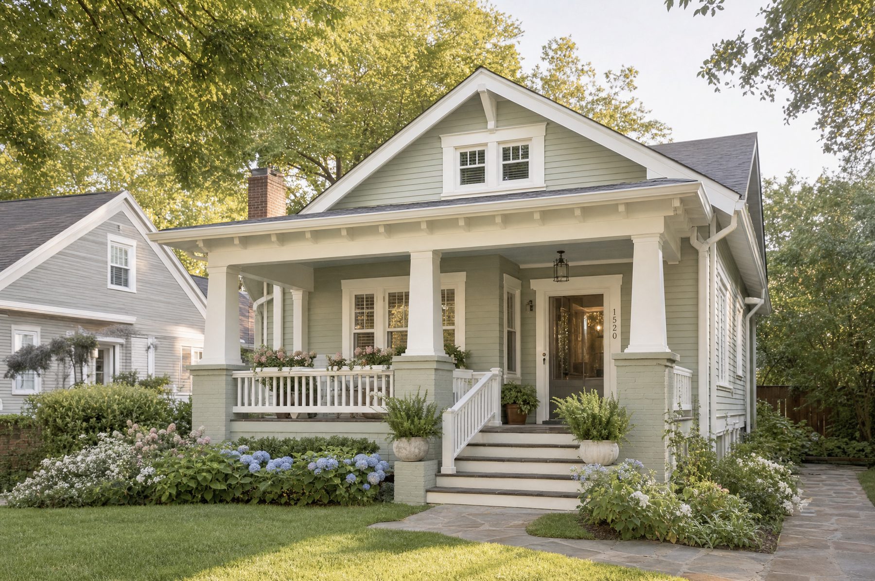 A sage-green craftsman home with a deep front porch and a mature tree